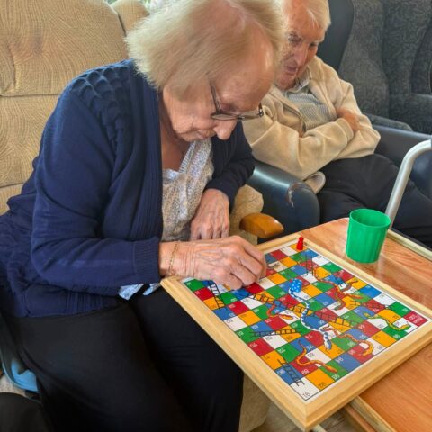 Resident playing a game of Snakes and Ladders at a table
