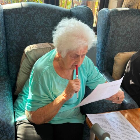 Resident reading an activity sheet while seated in the lounge
