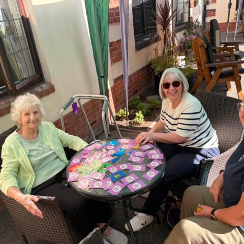 Resident and companions enjoying a card activity outdoors on the patio