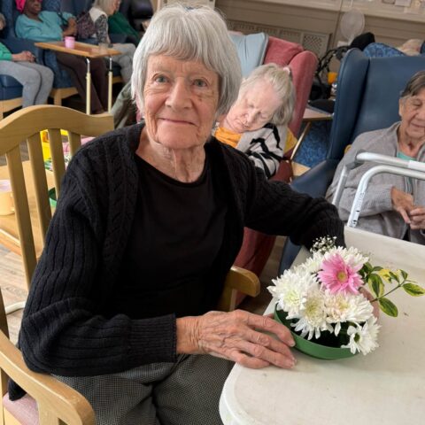 Resident smiling beside a completed white and pink flower arrangement