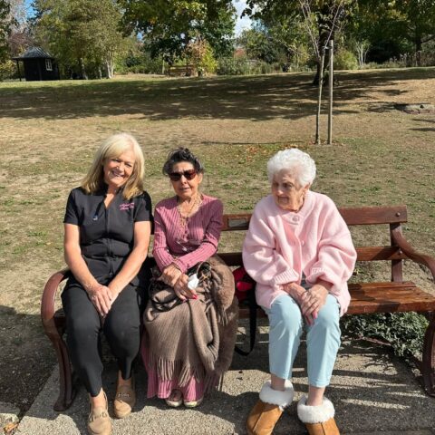 Care team member and residents smiling together on a park bench