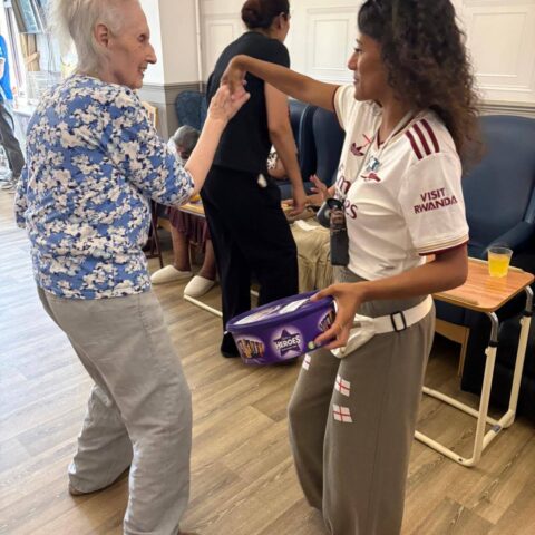 Two people holding hands at a community event, one holding a tub of chocolates.