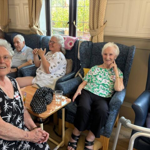 Older adults sitting together indoors in armchairs, enjoying a social moment.