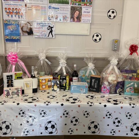 A table filled with wrapped gift baskets and raffle prizes at a community event.