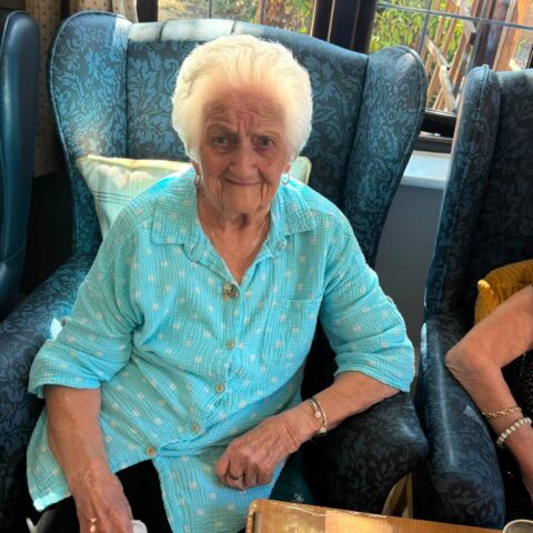 Resident wearing a turquoise top relaxing in an armchair beside the window