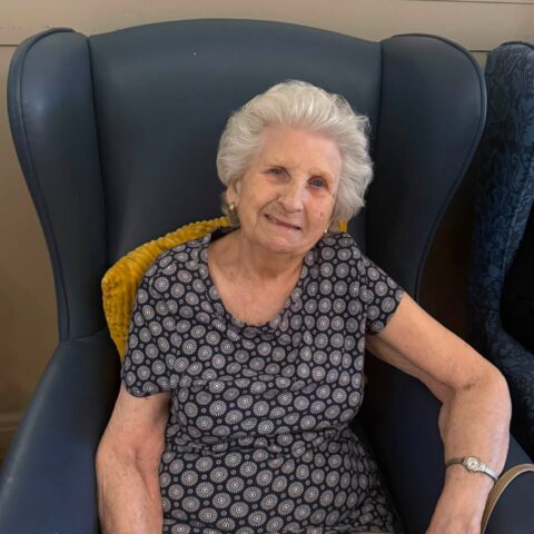 Resident smiling while relaxing in a comfortable armchair in the care home lounge