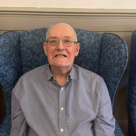 Male resident wearing glasses seated in a patterned armchair