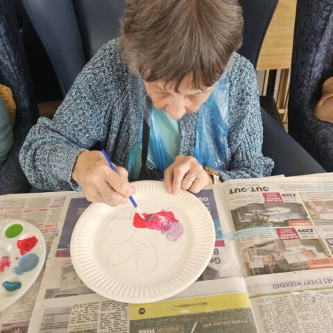 Resident painting a paper plate during an arts and crafts activity at Nightingale Care Home