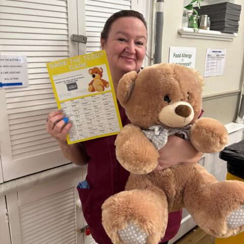 Smiling care team member holding a teddy bear and a printed certificate