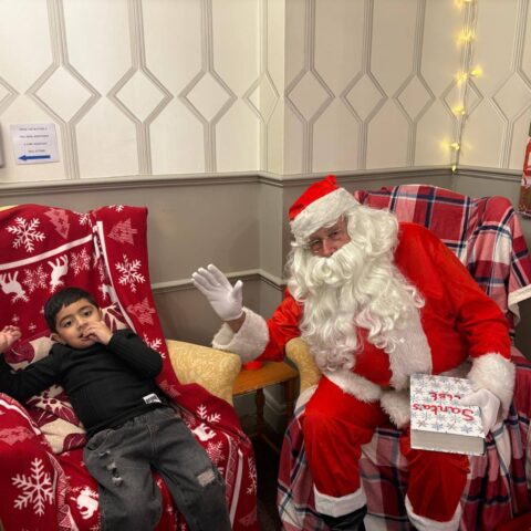 Young visitor seated beside Santa on a red Christmas chair