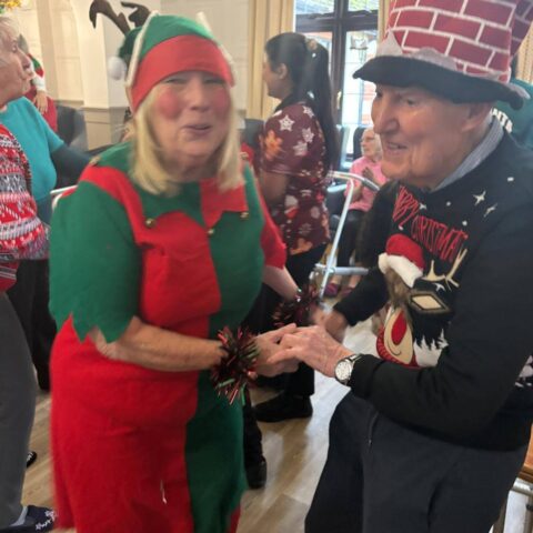 Christmas elf holding hands and dancing with a smiling resident