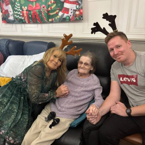 Resident seated between two smiling family members wearing festive antlers