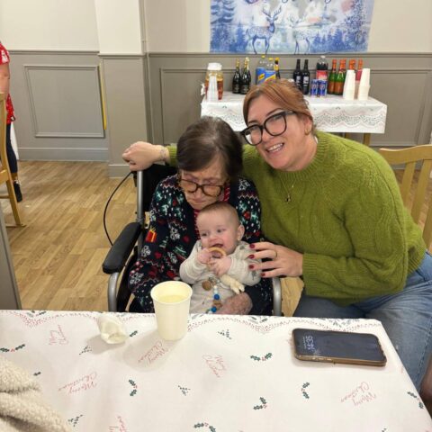 Two adults smiling with a baby at a table during the Christmas celebration