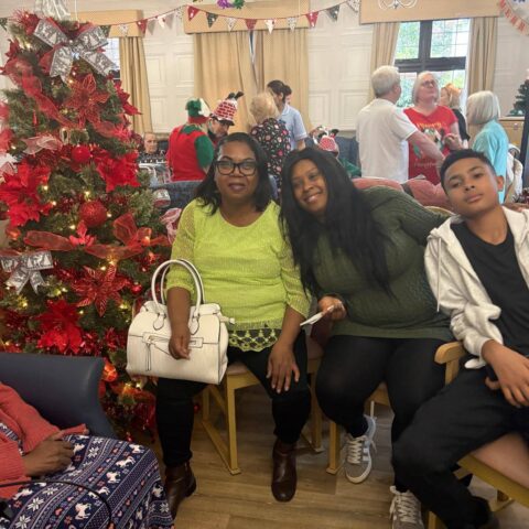 Three family members seated together beside a red decorated Christmas tree