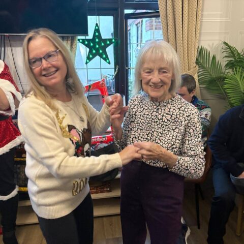 Resident holding hands with a smiling visitor during a festive dance