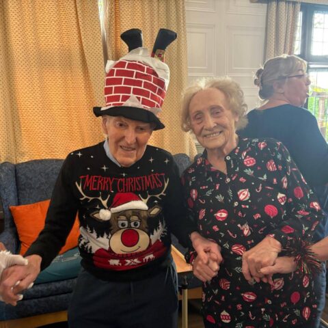Resident and visitor smiling together in colourful Christmas hats