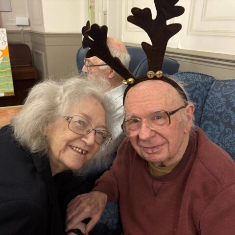 Smiling resident and visitor seated together wearing reindeer antlers