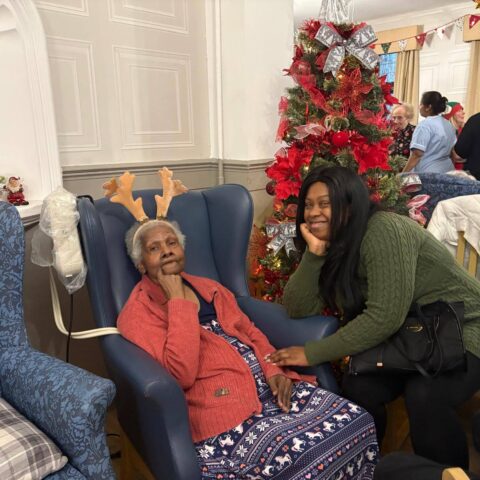Resident in festive reindeer antlers smiling with a visitor beside the Christmas tree