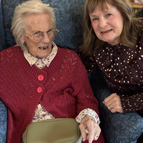 Smiling resident and visitor seated together in the decorated lounge