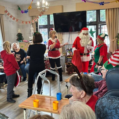 Residents team members Santa and an elf gathered in the decorated care home lounge
