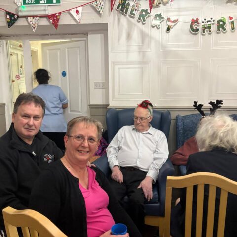 Two smiling visitors seated together beneath Christmas decorations