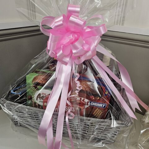 Cellophane-wrapped gift hamper with chocolate treats and a large pink bow