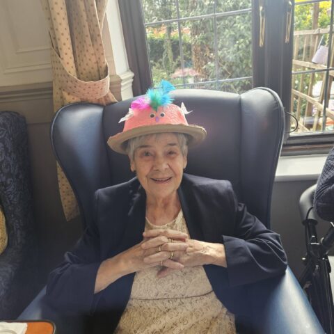 Smiling resident seated in an armchair wearing a handmade pink Easter bonnet