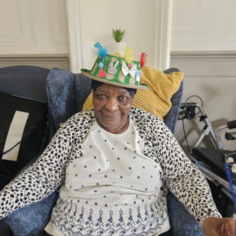 Smiling resident seated in the lounge wearing a handmade colourful Easter crown