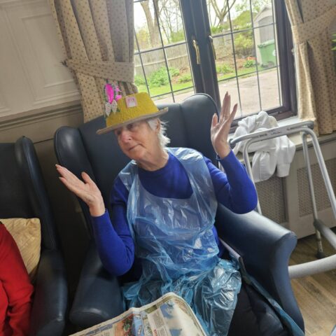 Resident seated in an armchair wearing a handmade blue Easter bonnet