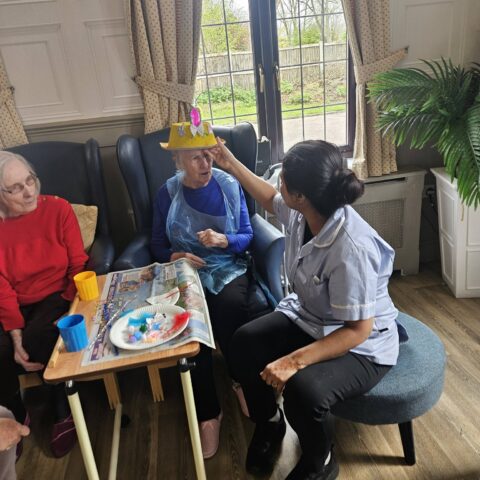 Care team member helping seated residents with decorated Easter bonnets at a table