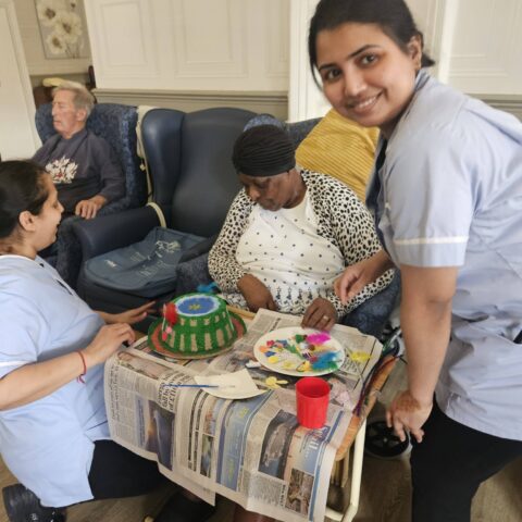Two care team members smiling with a resident and colourful handmade Easter bonnets
