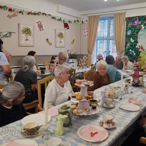 Residents gathered around a long table with cakes teacups and colourful themed decorations