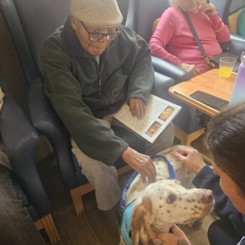 Resident reaching out to stroke a friendly visiting dog in the lounge