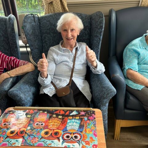 Resident giving two thumbs up beside a completed colourful owl jigsaw puzzle