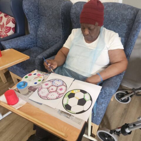 Resident wearing a red beanie painting football designs with watercolours