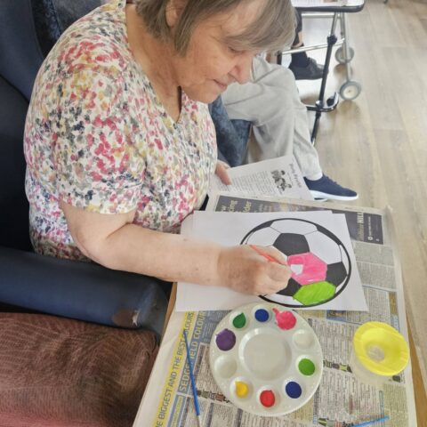 Resident painting a football design with pink and green watercolours