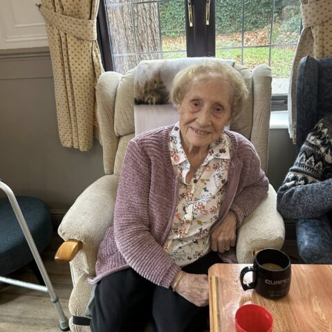 Smiling resident seated in a lounge chair beside a cup of tea