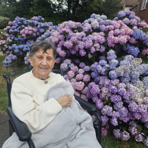 Resident smiling in a wheelchair beside purple and blue hydrangeas