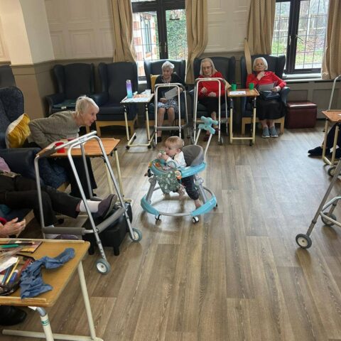 Residents seated around the lounge during a visit with a young child