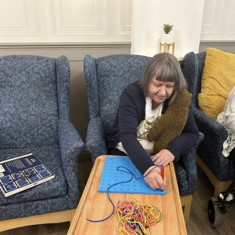 Resident seated at a table arranging colourful cords on a blue activity board
