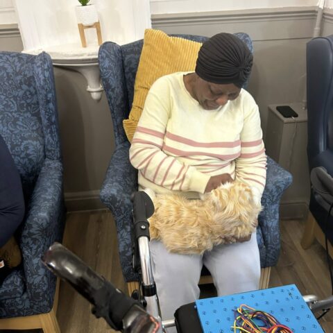 Resident seated in an armchair holding a soft sensory item beside a colourful activity board