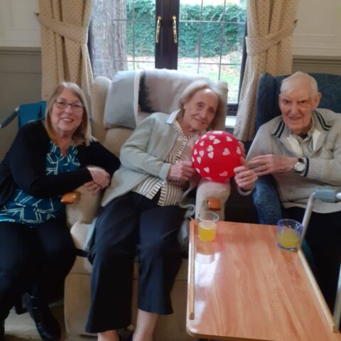 Three smiling people seated together with a red heart-patterned balloon