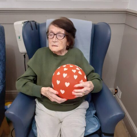 Resident seated in a blue armchair holding a red balloon decorated with white hearts