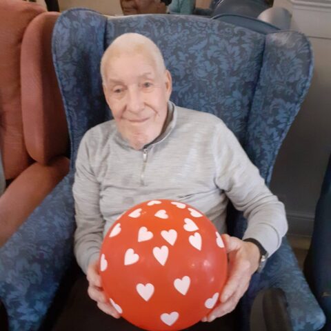 Smiling resident seated in an armchair holding a red heart-patterned balloon