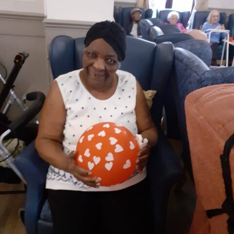 Resident seated in the lounge holding a red balloon covered with white hearts
