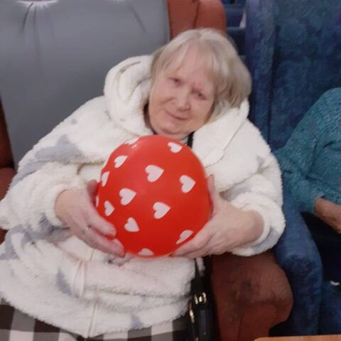 Resident in a light dressing gown holding a red balloon decorated with white hearts