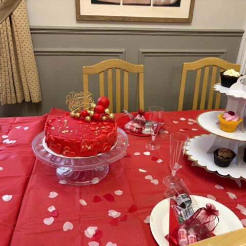 Red celebration cake and cupcakes displayed on a table scattered with heart decorations