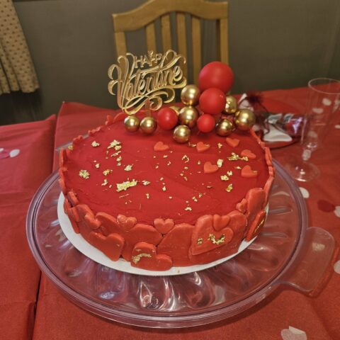 Red heart-themed celebration cake with gold decorations and a Happy Valentine topper