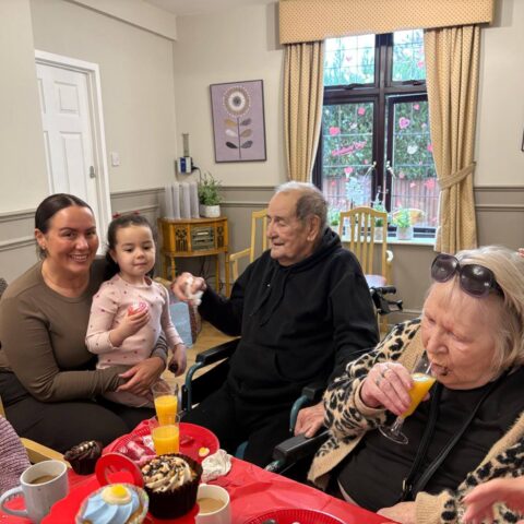 Family members and residents gathered around a decorated table with cakes and drinks