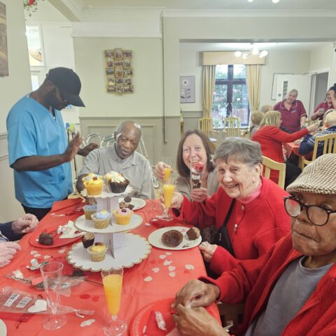 Residents gathered around a red decorated table with cupcakes and orange drinks